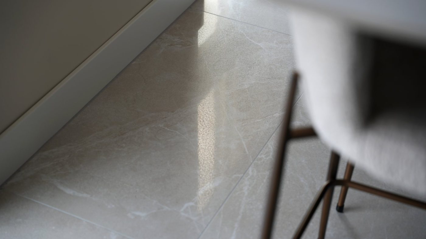 Detail van glanzende lichte marmerlook vloertegels in een woonkamer, met een eetkamerstoel