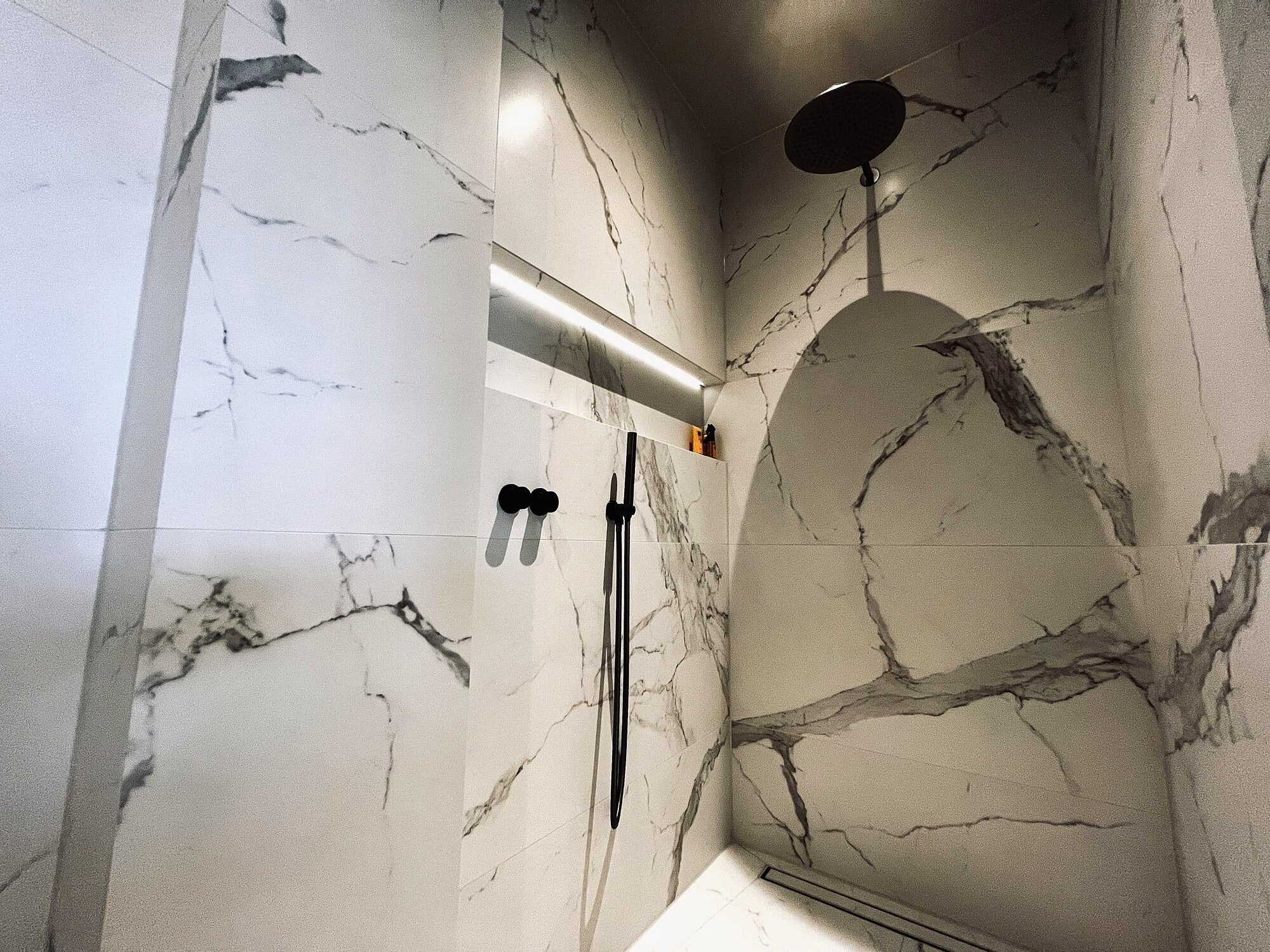 Badkamer met grote Calacatta-marmerlooktegels op wand en vloer en een inloopdouche
