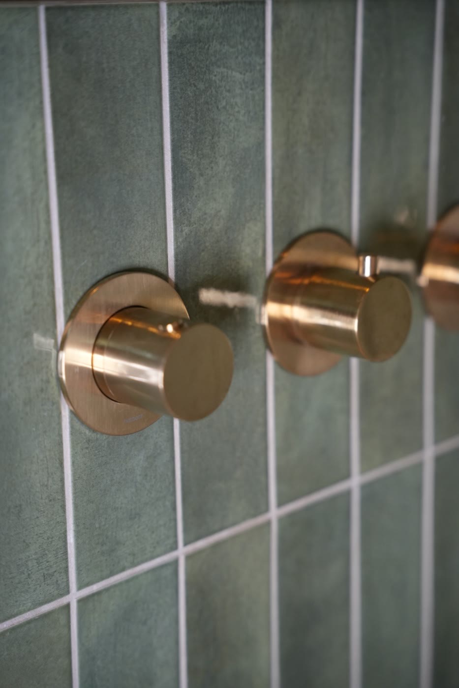 Badkamer met groene wandtegels en koperen kranen
