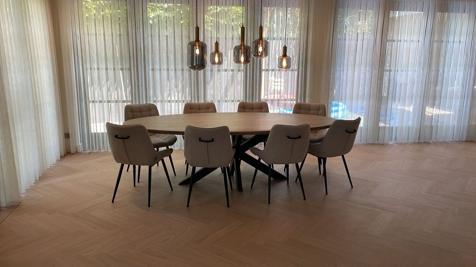 Eetkamer met een lichte visgraatvloer, een ovale eettafel en hanglampen