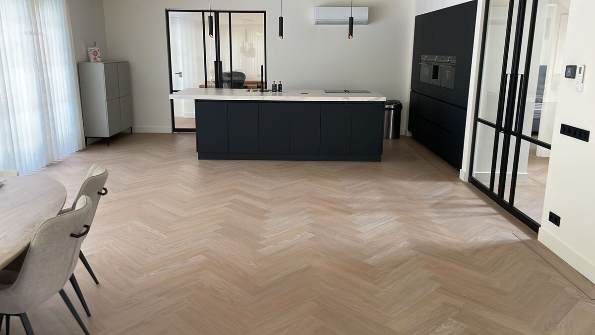 Open keuken met een zwart kookeiland en een lichte visgraatvloer