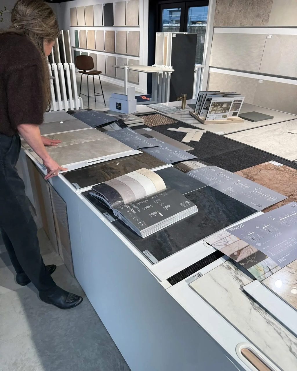 Een klant bekijkt tegelstalen en catalogi aan de tafel in de showroom