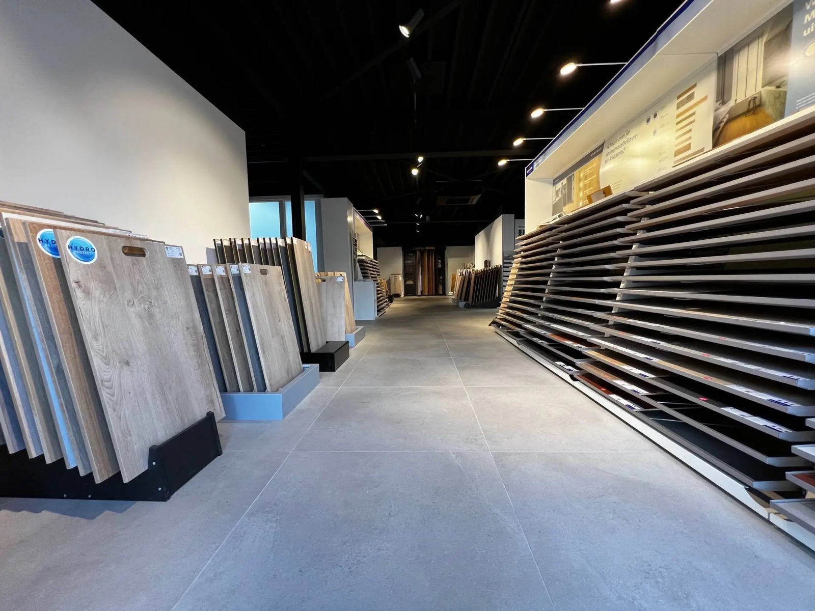 De vloerenafdeling in de showroom, met rekken vol pvc- en laminaatstalen en een grote tegelvloer