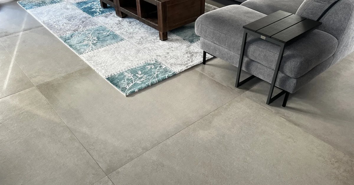 Woonkamer met een grote lichtgrijze betonlook tegelvloer, een bank en een vloerkleed