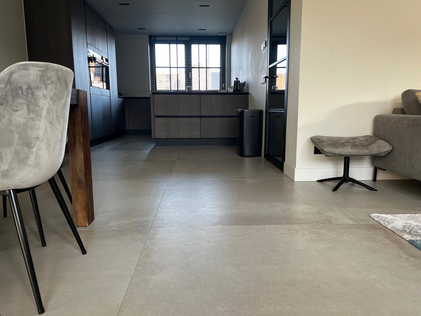 Woonkamer met open keuken en grote lichte betonlook vloertegels